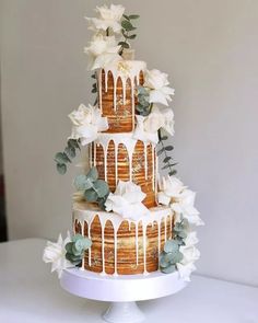 a three tiered cake with white flowers and greenery on the top is covered in icing