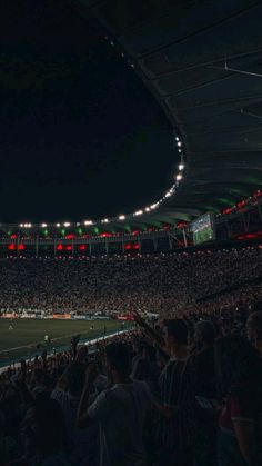 a stadium full of people at night with lights on the ceiling and fans in the stands