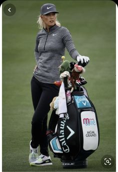 a woman holding a golf bag on top of a green field