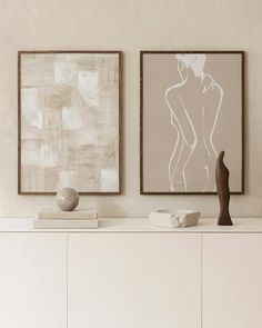 two abstract paintings hang on the wall above a white cabinet in a room with neutral walls