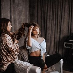 two women are sitting on a couch and one is combing her hair while the other sits down