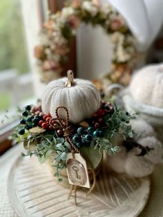 a white pumpkin sitting on top of a glass plate next to flowers and wreaths