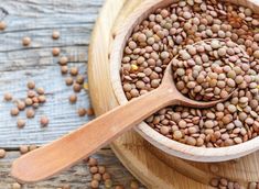 a wooden bowl filled with lentils on top of a wooden table next to a spoon