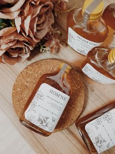 three bottles of honey sit on a cork coaster next to some flowers and paper tags