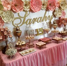 a table topped with lots of desserts next to a wall covered in paper flowers