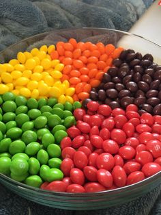 a bowl filled with different colored candies on top of a blanket next to a book