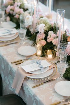 the table is set with white and pink flowers, gold rimmed plates, candles and napkins