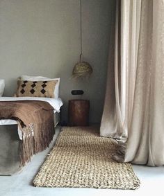 a bed sitting next to a window in a bedroom under a light brown blanket on top of a rug