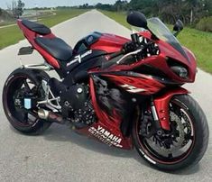 a red and black motorcycle parked on the side of a road in front of some grass