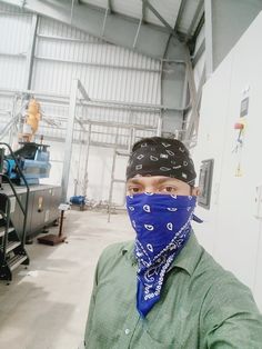 a man wearing a bandana in a factory with machinery behind him and his face covered by a mask