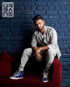 a man sitting on top of a red couch next to a blue brick wall and wearing sneakers