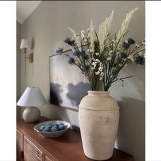 a white vase with blue flowers on a table next to a bowl and lamp in a room