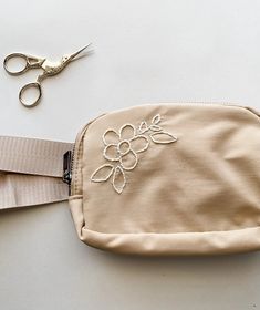 a pair of scissors sitting on top of a beige pouch with flowers embroidered on it