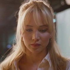 a woman with blond hair is looking down at her cell phone while wearing a white shirt