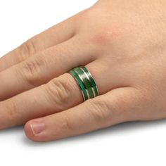 a person's hand with a green ring on their left and the other hand holding it