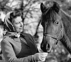 a woman is standing next to a horse and holding something in her hand while wearing a headscarf