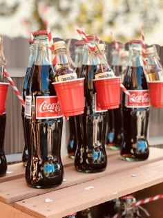 coca - cola bottles lined up on a table with paper straws in their cups