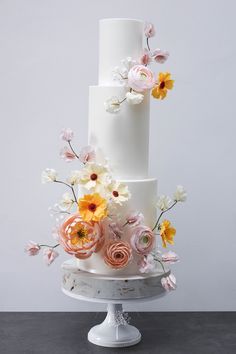 a three tiered white cake with flowers on it's side and the top layer is covered in icing