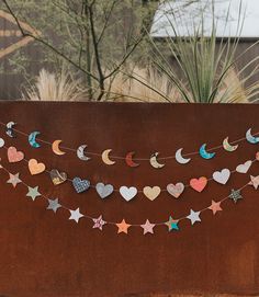 a string of paper hearts and stars on a brown wall with trees in the background