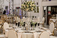 the tables are set for an event with white and gold chairs, silverware, and flowers