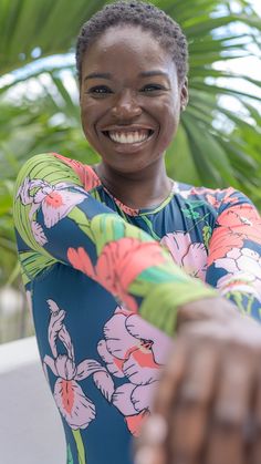 a smiling woman with her arms crossed and palm trees in the background