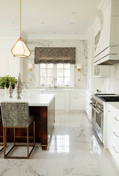 a white kitchen with marble counter tops and an island in front of a stove top oven