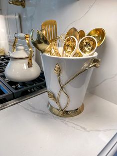 a white vase filled with gold spoons and forks on top of a counter next to a stove