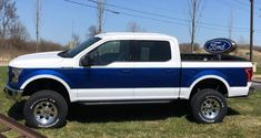 a white and blue ford truck parked in the grass next to a sign that says ford