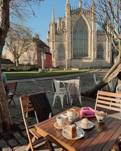 a wooden table topped with plates of food next to a tall church building in the background