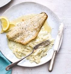 a white plate topped with fish and pasta next to a fork on top of a table