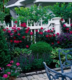 a garden filled with lots of flowers next to a white picket fence and blue chair