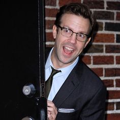 a man wearing glasses and a suit holding onto a door