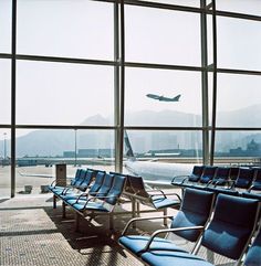 an airport terminal filled with lots of blue chairs and a plane in the sky behind them