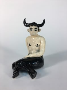 a ceramic figurine sitting on top of a black animal's leg and wearing horns