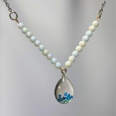 a necklace with a tear shaped glass bead hanging from it's center, surrounded by pearls