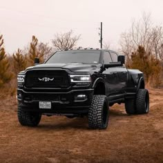 a large black truck parked on top of a dirt covered field with trees in the background