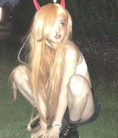 a woman with long blonde hair and devil horns on her head is kneeling in the grass