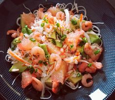 a black plate topped with shrimp, noodles and veggies on top of it