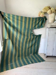 a green and yellow striped blanket sitting on top of a wooden floor next to a vase with flowers