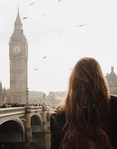 there is a woman that is looking at the big ben clock tower from across the river