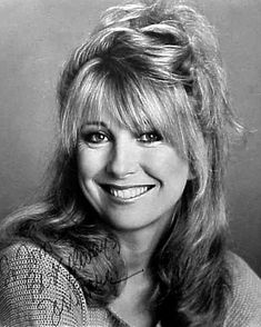 a black and white photo of a woman with long hair smiling at the camera while wearing a sweater