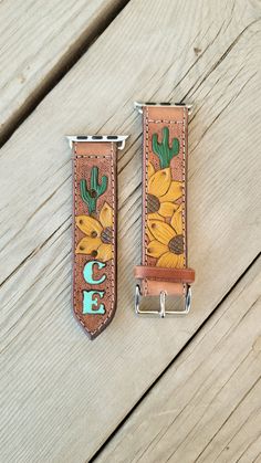 two leather straps with sunflowers and cactus on them sitting on a wooden surface