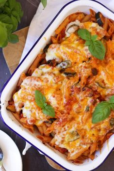 a casserole dish filled with pasta, cheese and spinach garnished with fresh basil