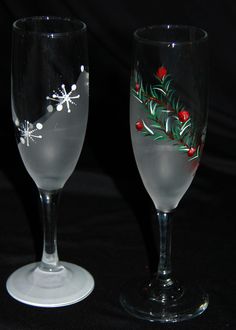 two wine glasses decorated with holly and red berries are sitting side by side on a black surface