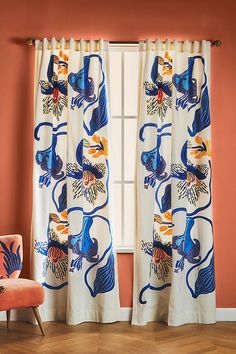 an orange chair sitting in front of a window covered in blue and white curtains with birds on them