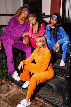 three women sitting on a bench wearing bright colored outfits and white sneakers, all looking at the camera