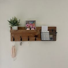 a wooden shelf with two hooks holding items and a potted plant on the wall