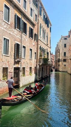 two people in a gondola on a canal with buildings and windows behind them