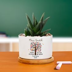 a small potted plant on a wooden table with two white crayons next to it