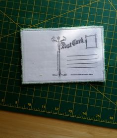 a piece of cloth with the word postcard on it sitting next to a ruler